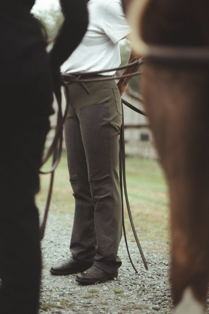 A rider in The Bushwacker in Moss stands on a gravel lane beside her horse